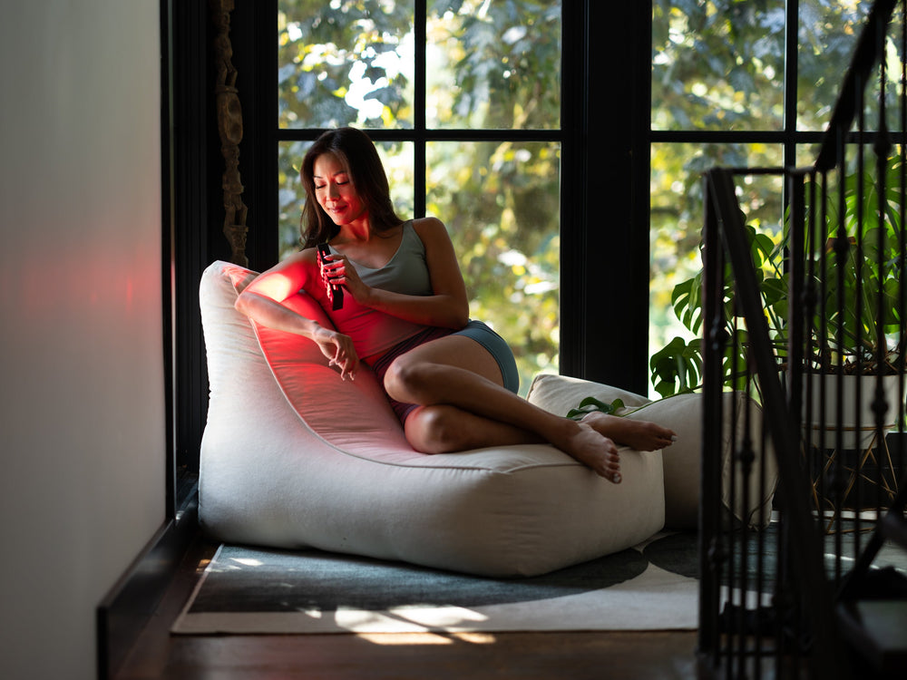 woman sitting on couch using Orion Edge 2 Red Light Therapy